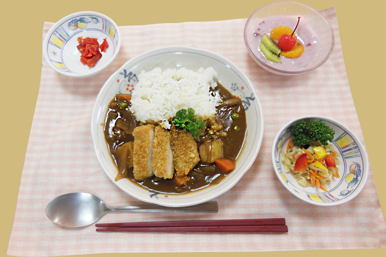 介護施設の食事。カツカレー、ライス、小鉢、デザートのセット